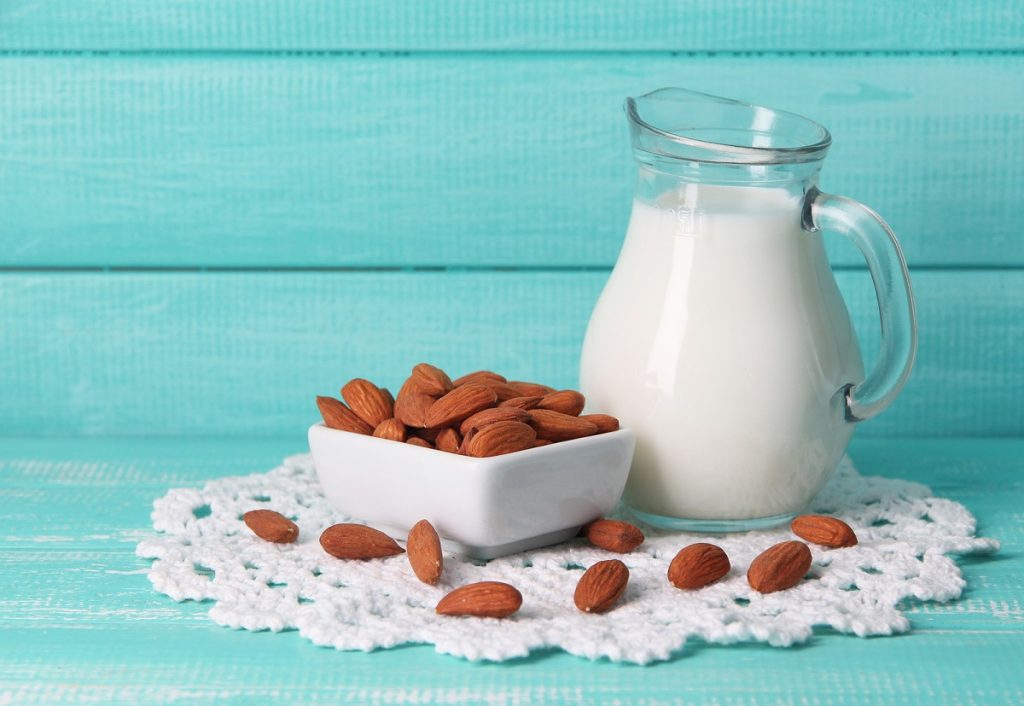 Almond milk in jug with almonds in bowl, on color wooden backgro
