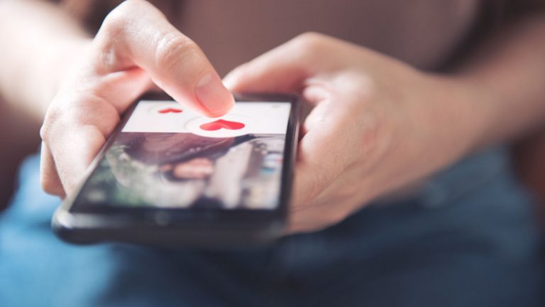 Finger Of Woman Pushing Heart Icon On Screen In Mobile Smartphone Application. Online Dating App, Valentine's Day Concept.