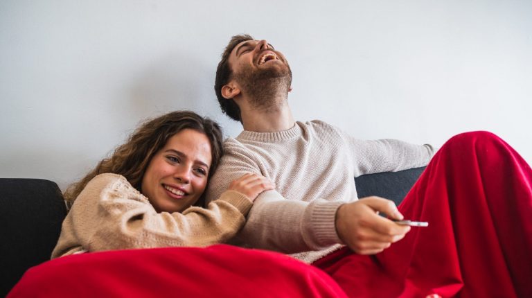 Cheerful Man And Woman Watching TV Covered With Blanket