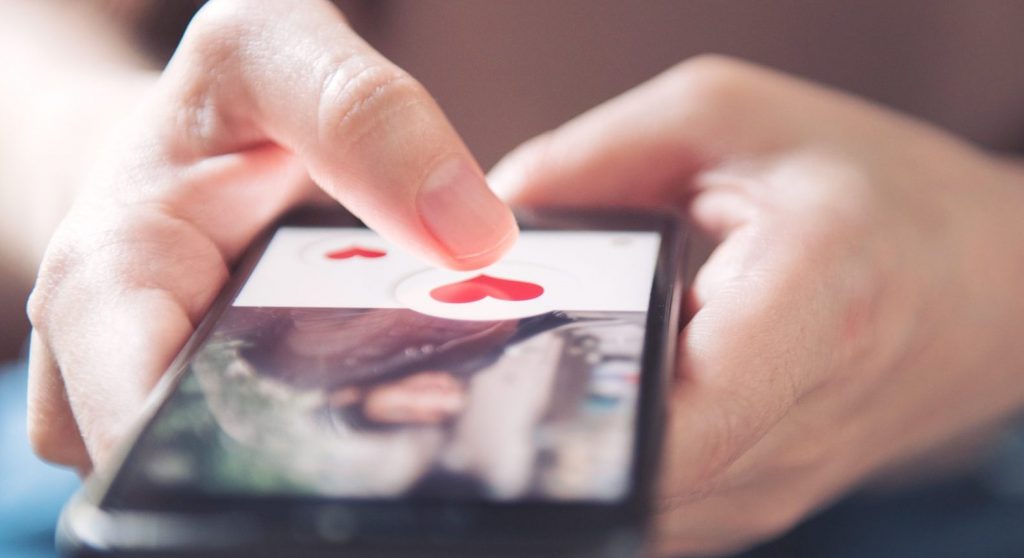 Finger Of Woman Pushing Heart Icon On Screen In Mobile Smartphone Application. Online Dating App, Valentine's Day Concept.