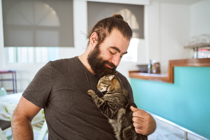 Positive Ethnic Guy Caressing Obedient Cat At Home