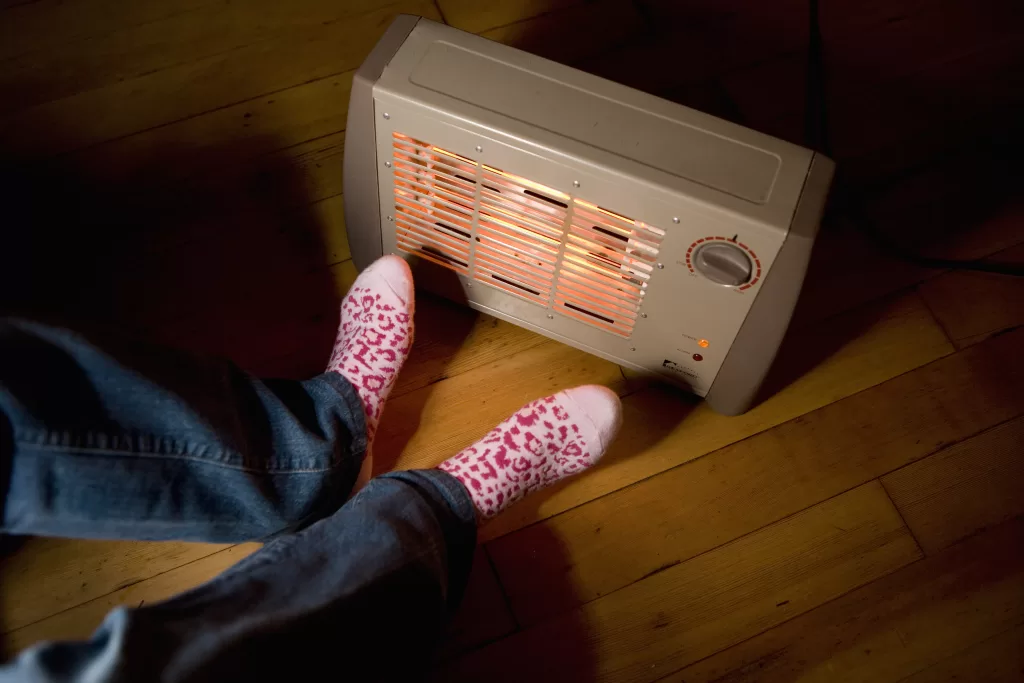 Teenage Girl (14 16) Warming Feet Beside Electric Heater, Low Section